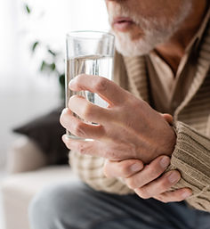 cropped view of aged man with parkinsonism holding glass of water in trembling hands while