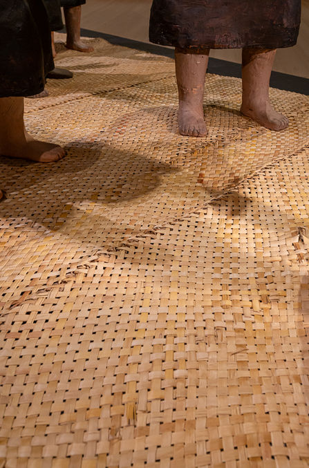 Close up of installation of life size ceramic figures of women and a child in the formation of a Māori karanga on flax mats.