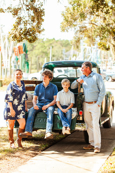 a family of four sitting and standing in the back of an old green truck smiling