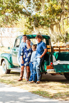 A family of four leaning up against an old green truck under the oak trees with Spanish moss