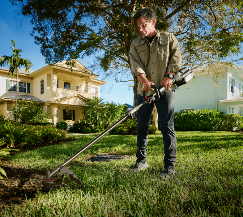 A person using a Kress KG164 electric trimmer to trim their grass, showcasing a clean and quiet alternative to gas-powered tools.