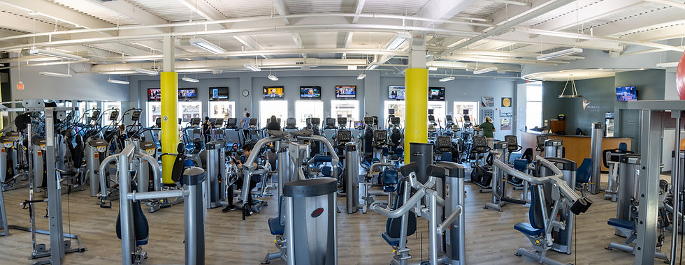 Gym interior with numerous exercise machines, several people using treadmills. TVs on walls display news. Bright, spacious setting.