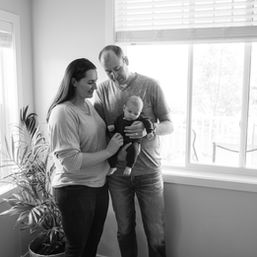mother and father holding newborn baby while standing in front of living room window