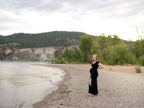 pregnant mom wearing a black dress poses on a beach at sunset for a maternity photoshoot