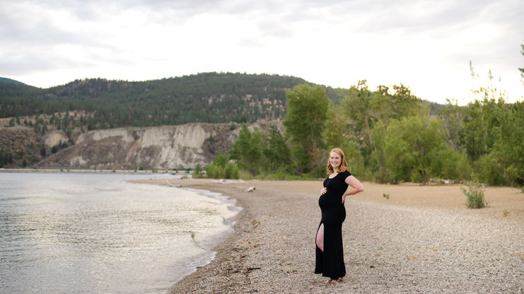 pregnant mom wearing a black dress poses on a beach at sunset for a maternity photoshoot