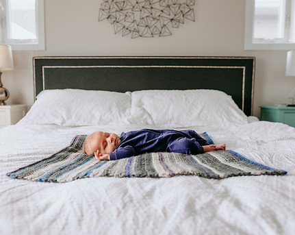 Newborn baby laying on bed for lifestyle photography in Penticton