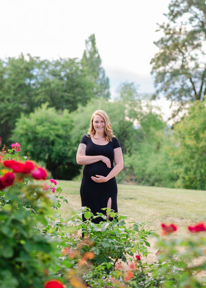 Pregnant mother in a black dress psoing in a rose garden for a photoshoot. Okanagan Maternity photoshoot at the Summerland Ornamental Gardens