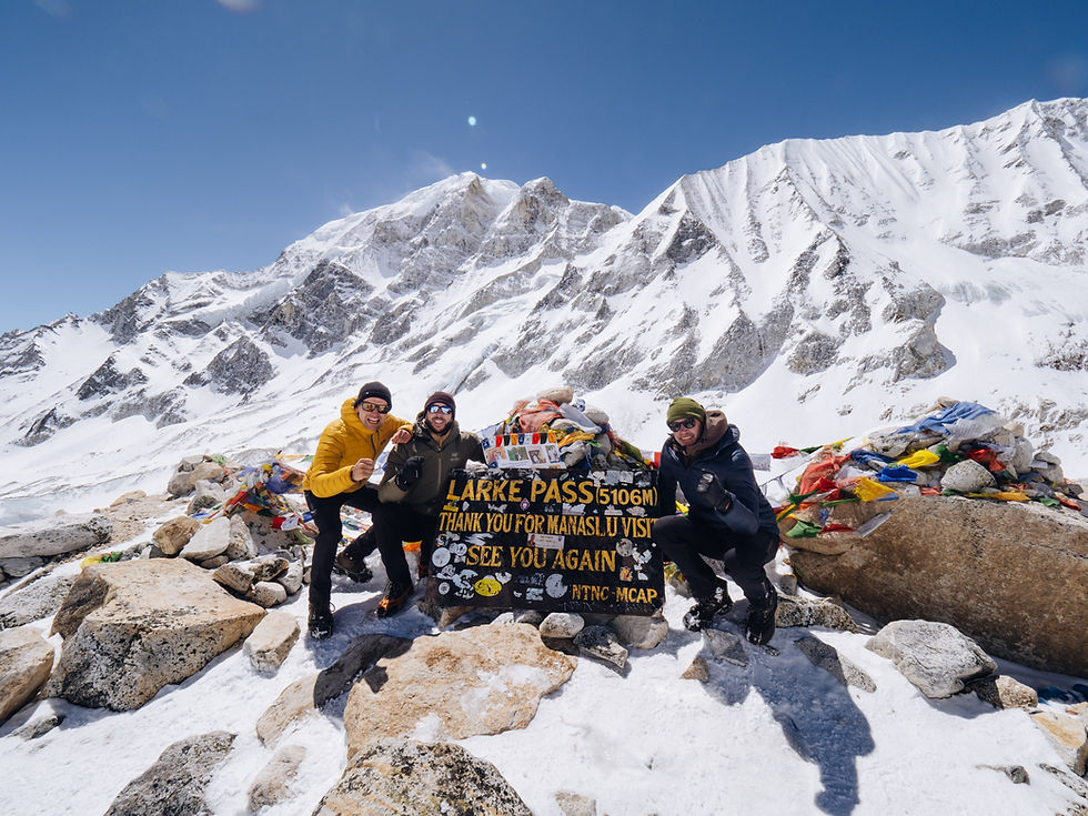 Drie bergbeklimmers poseren bij bord Larke Pass (5106 m) in besneeuwde Himalaya onder heldere blauwe lucht op Manaslu Circuit tijdens een NOMADventure tocht