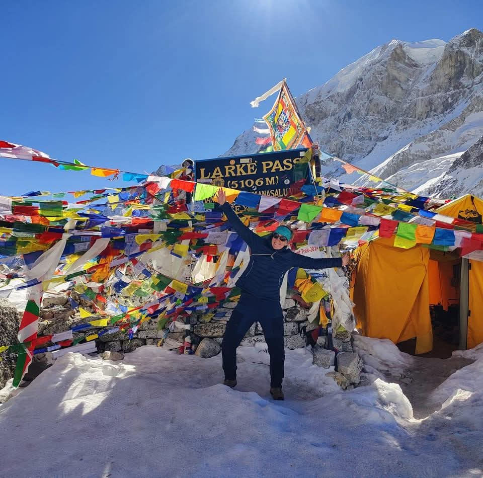 Wandelaar op de larke pas op het Manaslu circuit. Er zijn nepalese vlaggetjes en sneeuw. Ze is blij en juicht.