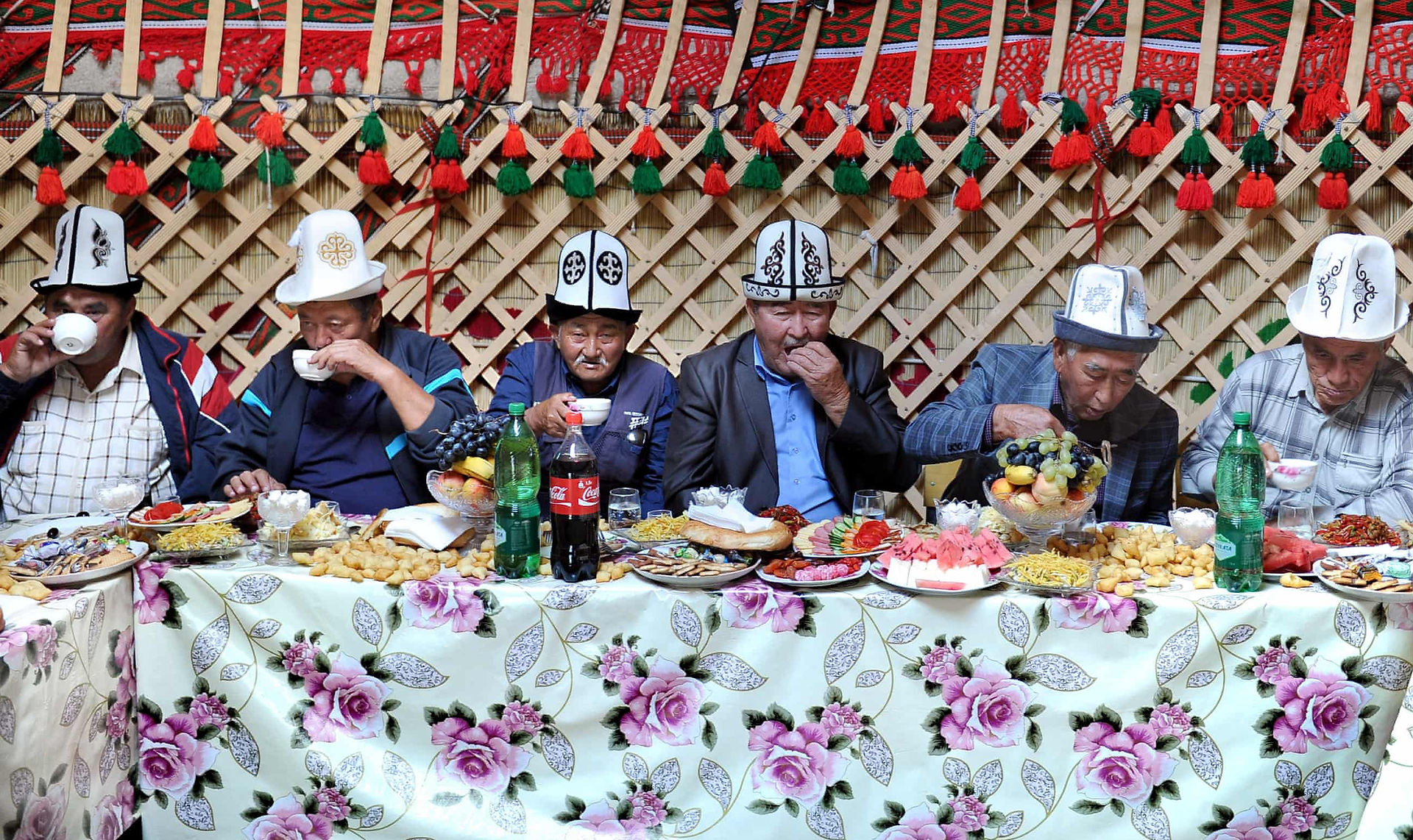 Mannen eten in traditionele kledij aan een Kirgizische buffettafel