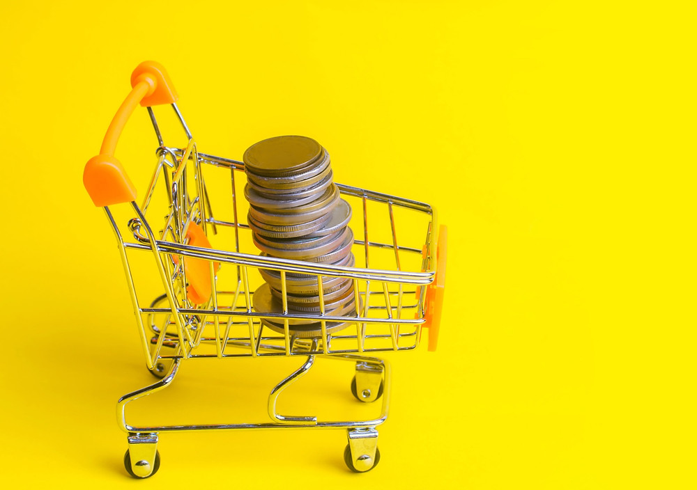 carrinho de supermercado pequeno em um fundo amarelo com moedas dentro