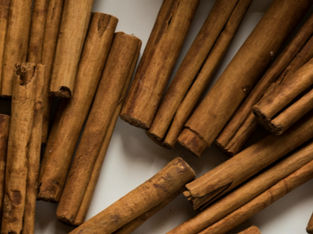 Cinnamon sticks scattered on a white surface, showing a warm brown color and texture.