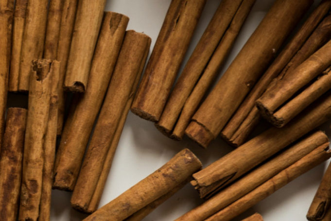 Cinnamon sticks scattered on a white surface, showing a warm brown color and texture.