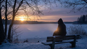 Hooded figure sits on snowy bench by a frozen lake at sunrise. Trees frame the serene scene, conveying solitude and tranquility. Winter’s Reduced Light: How Does It Influence Digestive Rhythm?