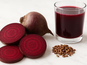Sliced beetroot, a whole beet, seeds, and a glass of beet juice on a white marble background. Rich red hues dominate the scene.