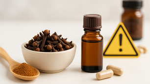 Bowl of cloves, brown bottle, capsules, and spoon of spice on white surface. Warning sign and jar in the background. Neutral mood. Herbpy Blog.