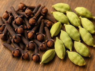 Close-up of brown cloves and green cardamom pods on a wooden surface, showcasing vibrant natural textures and colors.