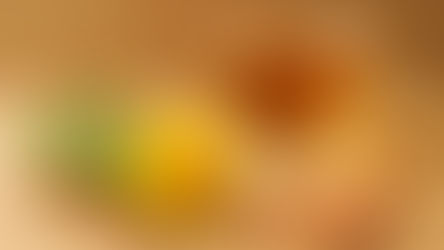 Dandelion flower, root, and cinnamon sticks on a wooden surface; a glass cup filled with golden brown tea in the background. Warm tones.