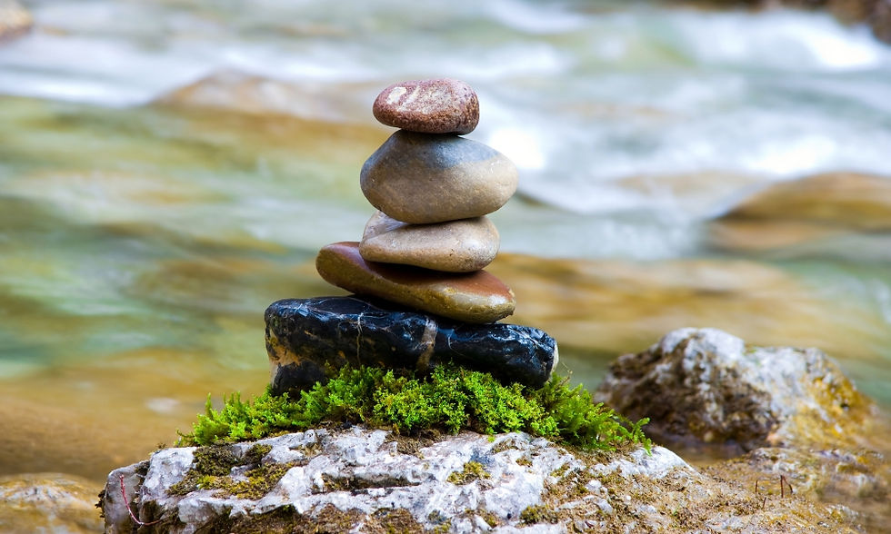 St. John’s Wort for Seasonal Mood Transition: Fall into Balance. Stacked stones on mossy rock by a flowing river. Smooth pebbles vary in color, set against blurred water, suggesting calm and balance.