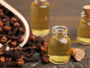 Small glass bottles with yellow oil and corks, surrounded by cloves on a wooden surface. Warm tones create a cozy, aromatic mood.