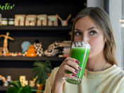 Woman in a cream sweater drinks green juice in a modern shop with shelves of products. The word "Detox" is visible. Calm mood. New Year Detox Prep (Green Tea): Fresh Start Power