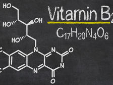 Chemical structure of Vitamin B2 chalk-drawn on a blackboard with yellow highlights. Text reads: "Vitamin B2, C17H20N4O6." Source: Canva