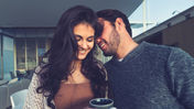Smiling couple indoors, man whispers to woman holding a coffee cup. Cozy mood with soft lighting, modern background. Saw Palmetto and Tribulus for Men’s Vitality