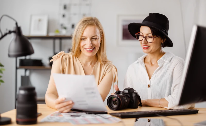 Une femme photographe qui photographie un jeune couple et un bébé devant leur maison.