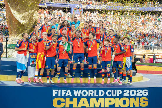 Soccer team in red jerseys celebrates on podium amid confetti, holding medals under FIFA World Cup 2026 Champions sign.