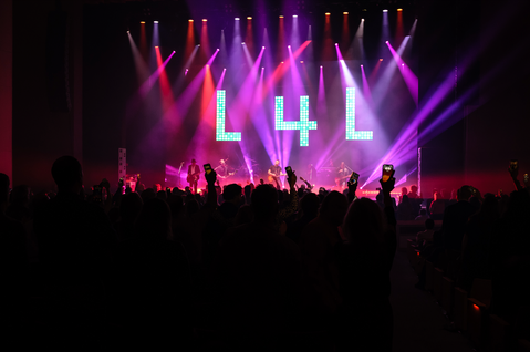 Photo from back of the crowd crowd during the event, with a big L-4-L lit up on stage. 
