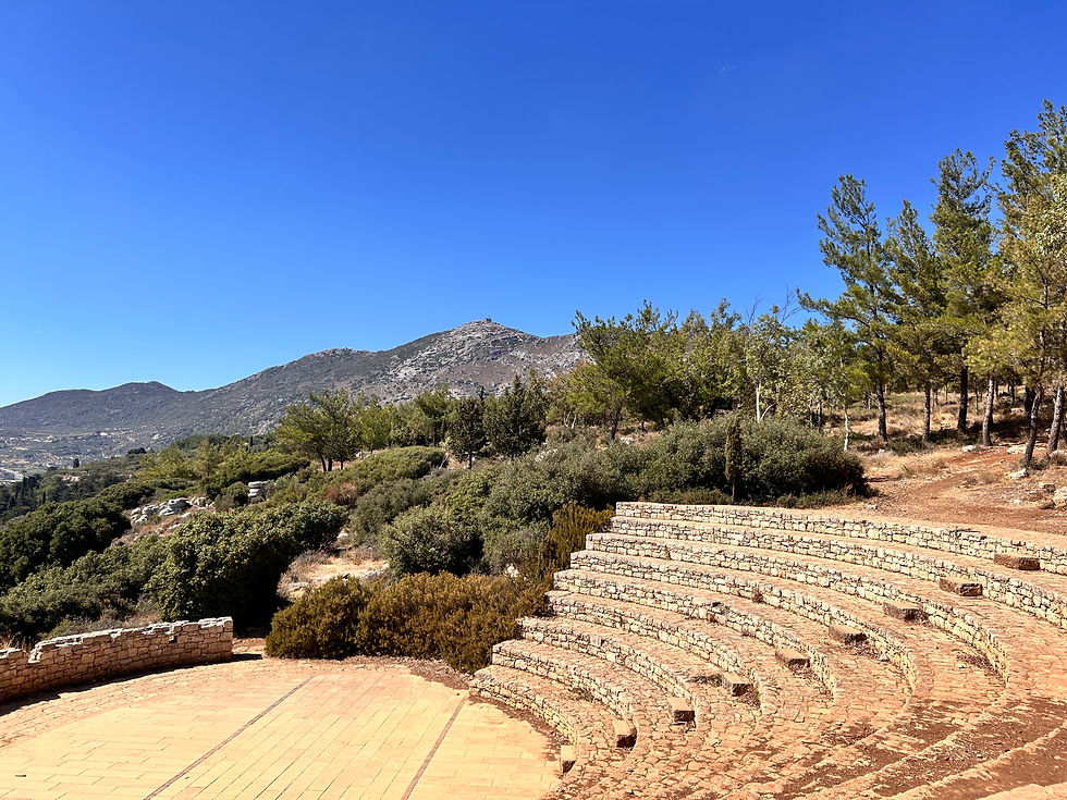 Steinernes Freilufttheater auf Kreta mit halbkreisförmigen Sitzreihen, im Hintergrund Pinien und Berge unter klarem blauem Himmel.