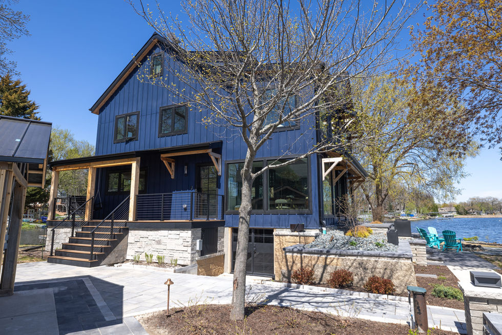 Modern lake house exterior with navy blue board and batten siding, large picture windows overlooking water, rustic cedar corbels, soffits, and beams