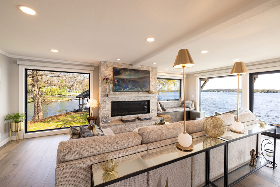Modern lake house living room with natural stone fireplace and floor-to-ceiling windows overlooking the water