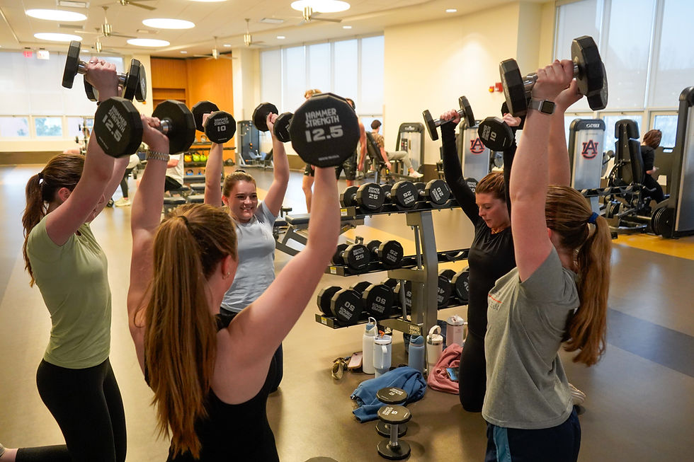 Girls in a circle lifting weights above their heads.