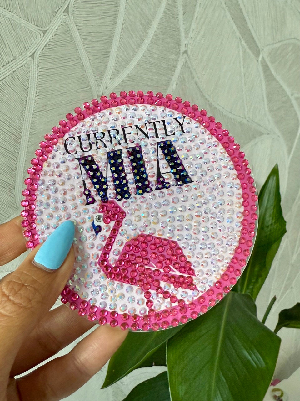 A sparkling rhinestone coaster with a pink flamingo and "Currently MIA" text, placed on a stylish wooden tray with a glass.