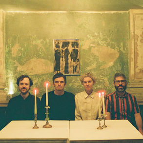 This is the cover for Modern Nature's, The Heat Warp album showing the band sitting at a table with lit candles in front. The green, distressed and textured wall and abstract art create an arty, alternative atmosphere.