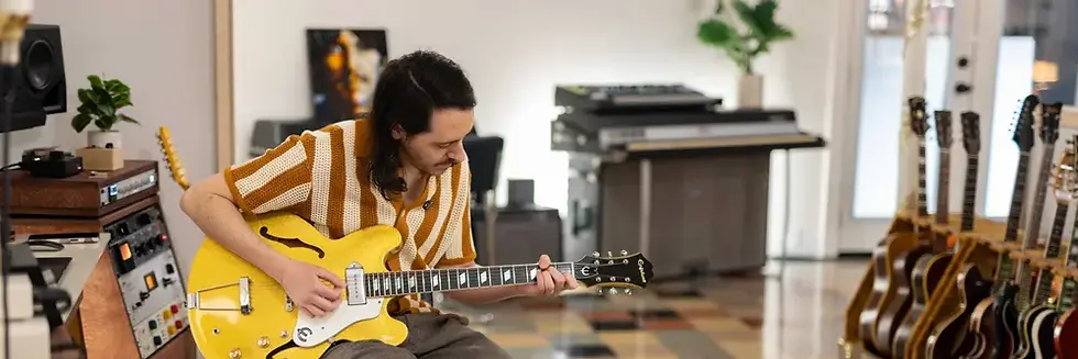 Nashville's SteveStout playing a yellow electric guitar in his Shabby Road music studio, with rows of guitars and gear around him.