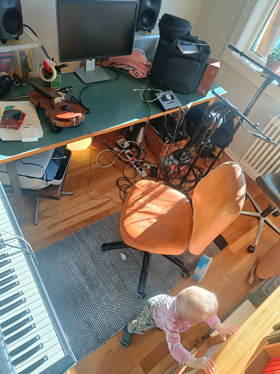 Cisser Maehl's home studio - a cluttered music desk with violin, monitor speakers, and cables in sunlight, next to a keyboard.