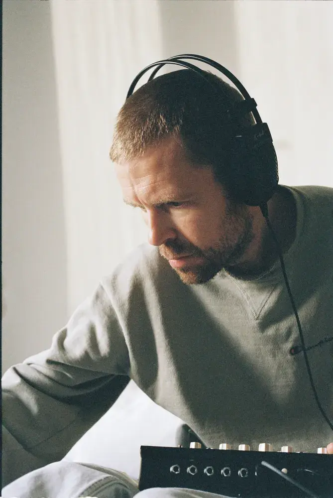 Joakin Frosgren aka Autorhythm wearing headphones leans over an audio mixer in a bright room, focused on adjusting controls.