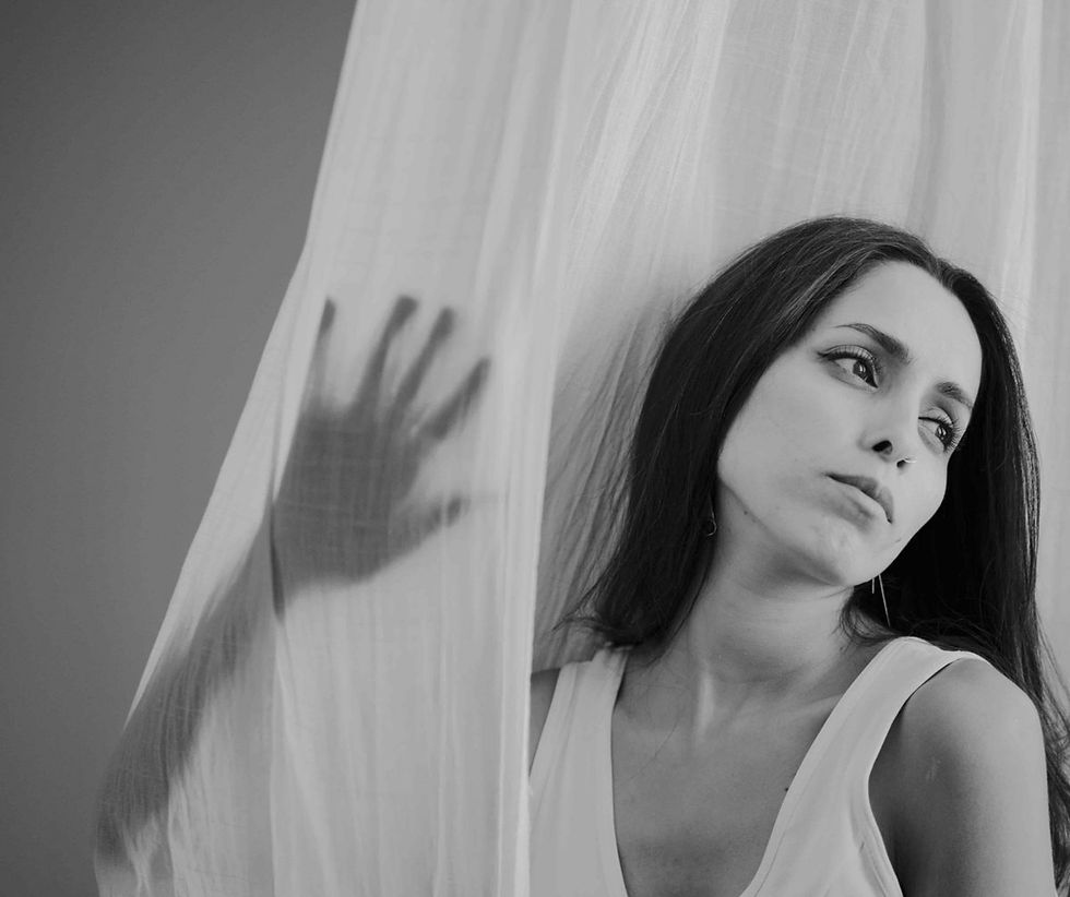 Salway Jaradat with long hair looks to the side, appearing thoughtful, behind a sheer curtain with a hand shadow. Black and white photo, calm mood.