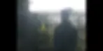 Casha Mour in dark clothing and a white capstands by a spiked fence in an outdoor setting. The sky is overcast, creating a subdued mood.