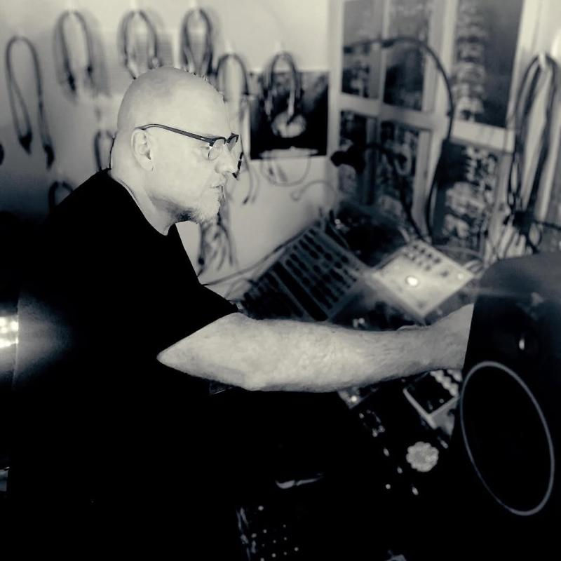 Brendon Moeller in glasses working in a sound studio, adjusting equipment. Background shows cables and panels. Moody black and white setting.