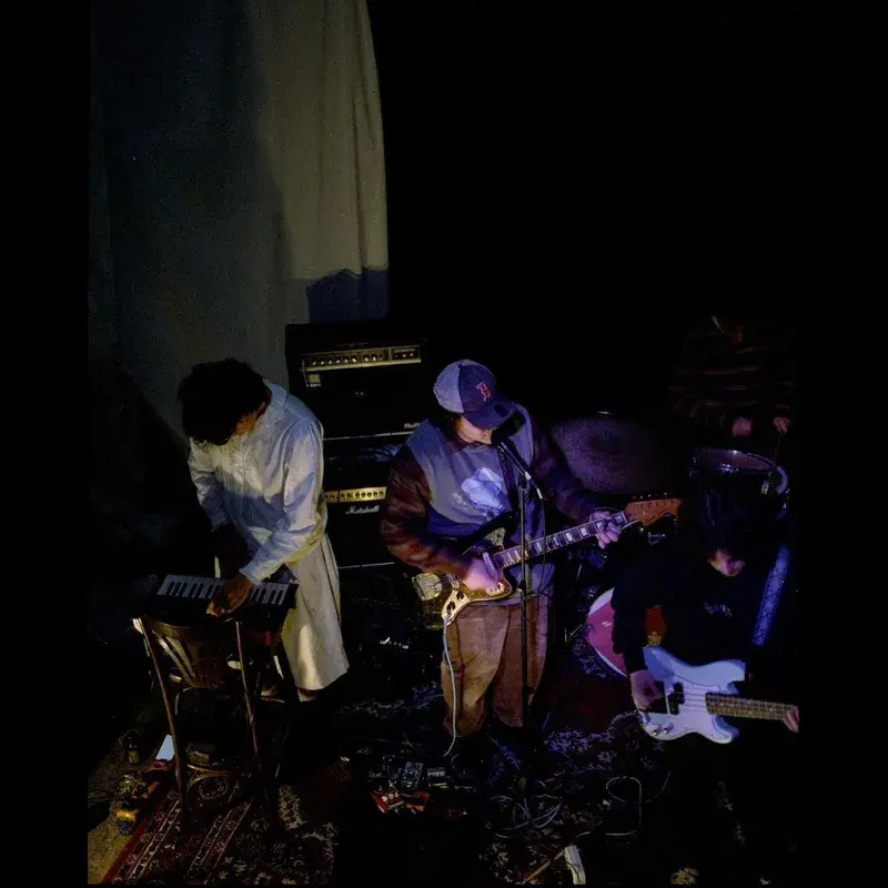 Munich indietronic group plainhead perform in a dark rehearsal room, one on keyboard, one on electric guitar, one on bass, with amps and cables around them.