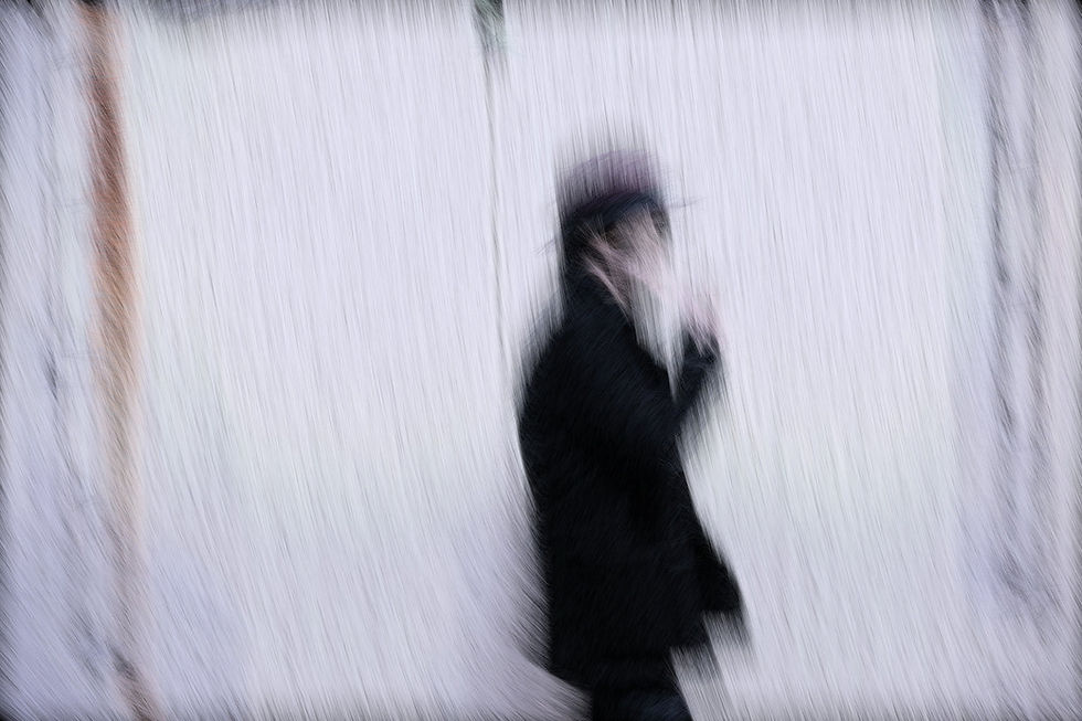 Japanese music producer Hiromu Yamaguchi in a black coat walking through falling snow, with pale white background and motion-streaked trees, creating a chilly, abstract and mysterious mood
