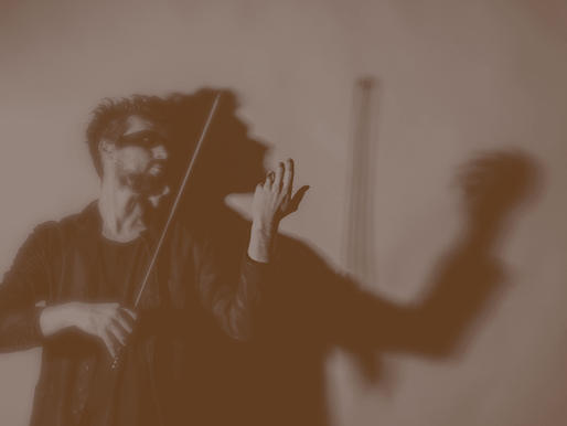 David Handlre playing an invisible violin, casting dramatic shadow on wall. Sepia tone creates a moody, artistic atmosphere.