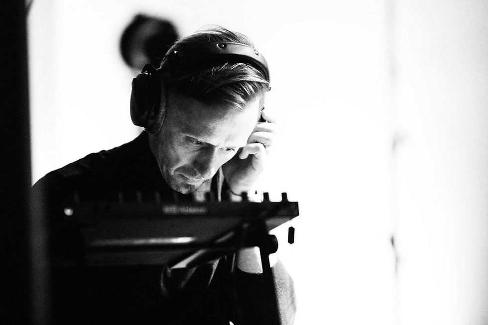 Lithuanian pianist, composer and producer Darius Žičkus with headphones focuses intently on music production equipment in a minimalist, black-and-white setting, creating a contemplative mood.