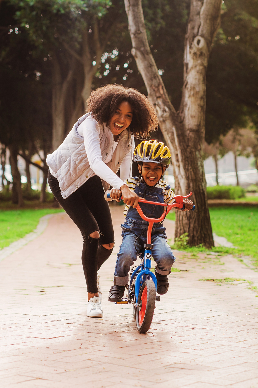 Una mujer negra ayuda a un niño negro a aprender a andar en una bicicleta roja.