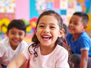 Una niña joven en la escuela sonríe ampliamente. Dos niños pequeños están sonriendo detrás de ella.