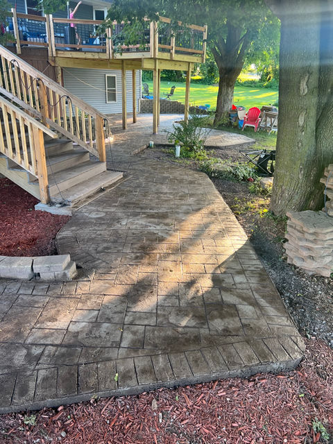 A photo of a concrete patio and wooden deck, showing a stamped design and color sealing in the concrete. 