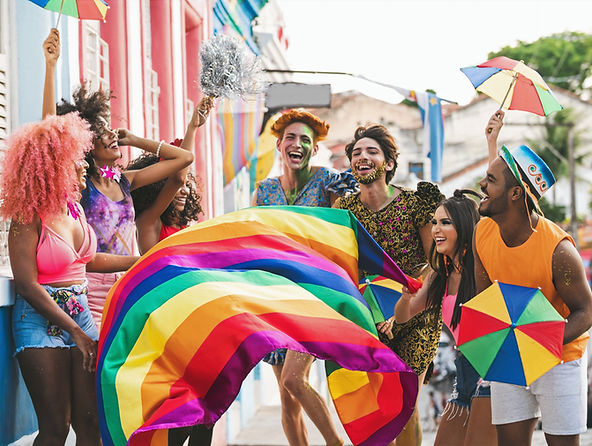 Group of joyful people celebrating outdoors with rainbow flags and colourful umbrellas at a Pride event